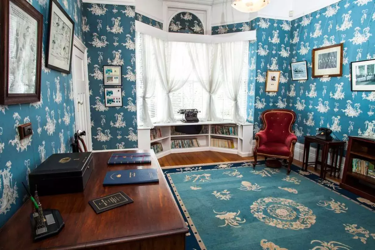 The office at Home Hill with vivid blue wallpaper, a bay window, timber furniture, blue carpet and pictures on the walls. 