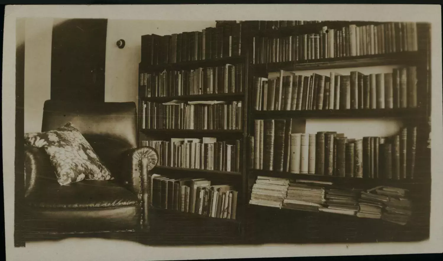 A leather armchair with a cushion and a large bookcase.  